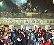 feiernde, jubelnde Menschen stehen vorm Brandenburger Tor, Feuerwerk fliegt in den Nachthimmel 