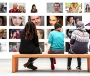 drei kinder sitzen auf einer Bank und betrachten eine riesige Fotowand mit Gesichtern