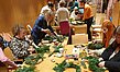 Frauen binden Weihnachtskränze an einem Tisch. Alle Utensilien und Tannenzweige liegen bereit.
