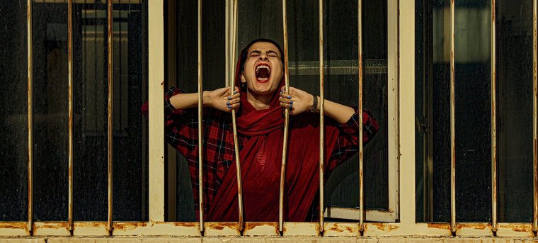 Eine Frau zieht Gitterstäbe auseinander und schreit nach draußen