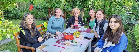 Teamfoto des Bür.A-Teams. Alle sitzen zusammen am Garten uns besprechen das Programm der Bür.A.