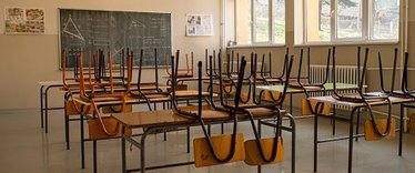 Blick in altes Klassenzimmer. Die Stühle sind auf die Tische geräumt. Der Raum ist leer.