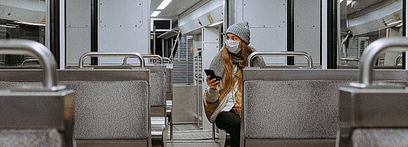 Leerer Straßenbahnwagon von innen. Nur eine Mitfahrerin sitzt alleine mit Maske im Wagon.