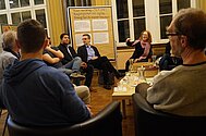Teilnehmende sitzen an einem Tisch mit Brezel und Obst. Die Gruppe ist im Gespräch