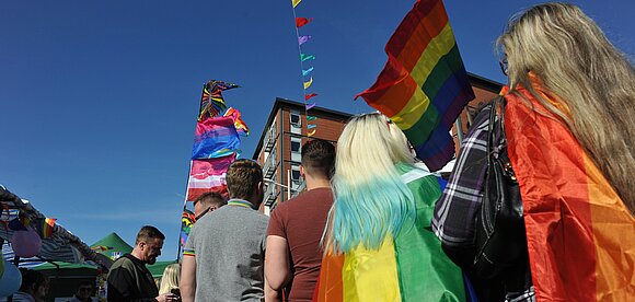 unter abendlichem Himmel versammeln sich viele Menschen, die die Regenbogenfahne tragen,