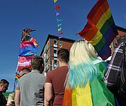 unter abendlichem Himmel versammeln sich viele Menschen, die die Regenbogenfahne tragen,