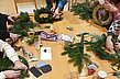 An einem Tisch werden Weihnachtskränze gebunden. Alle Utensilien und Tannenzweige liegen bereit.