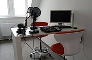 Tisch mit zwei Studoimikrophonen, Mischpult und PC. Hier werden die Podcastaufnahmen gemacht.