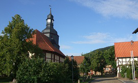 Blick auf eine Dorfstraße mit kleiner Kapelle und Fachwerkhäusern.
